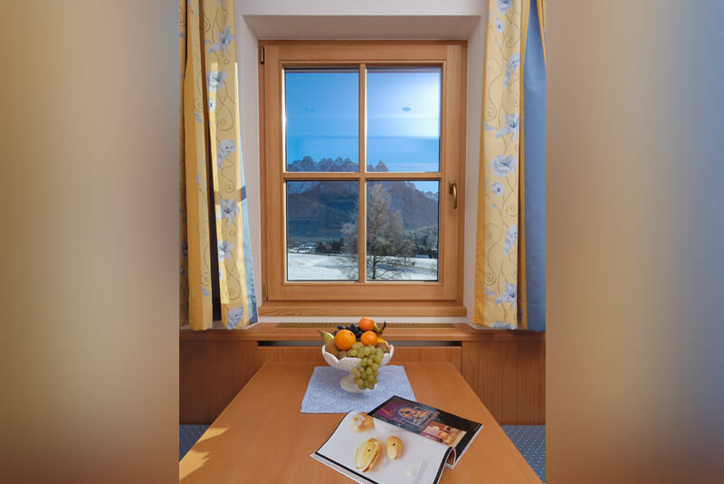 Dining table with a view through the window to the snowy Dobbiaco from holiday flat A - Hotel Hubertushof
