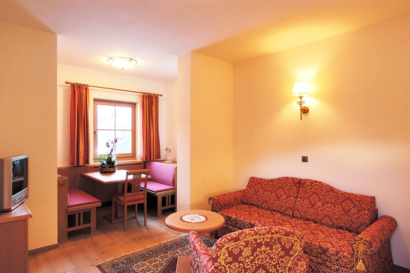 Living room with TV and table - holiday flat B - Hotel Hubertushof